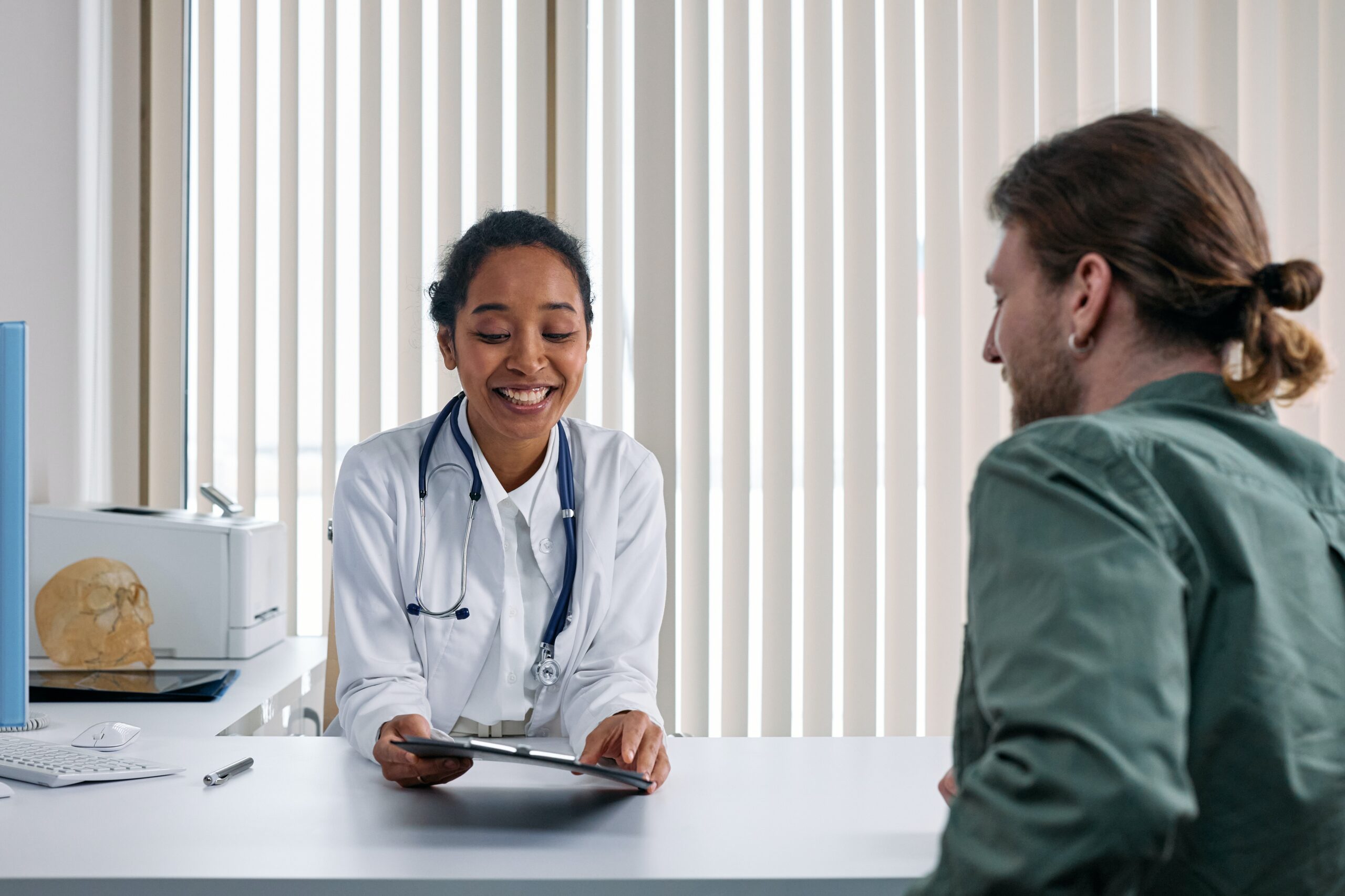 A doctor sits at a desk speaking to their patient